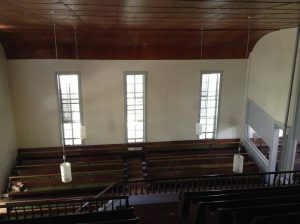 photo of a white wall with large windows and a brown curved section where the wall reaches the ceiling. rows of benches are below.